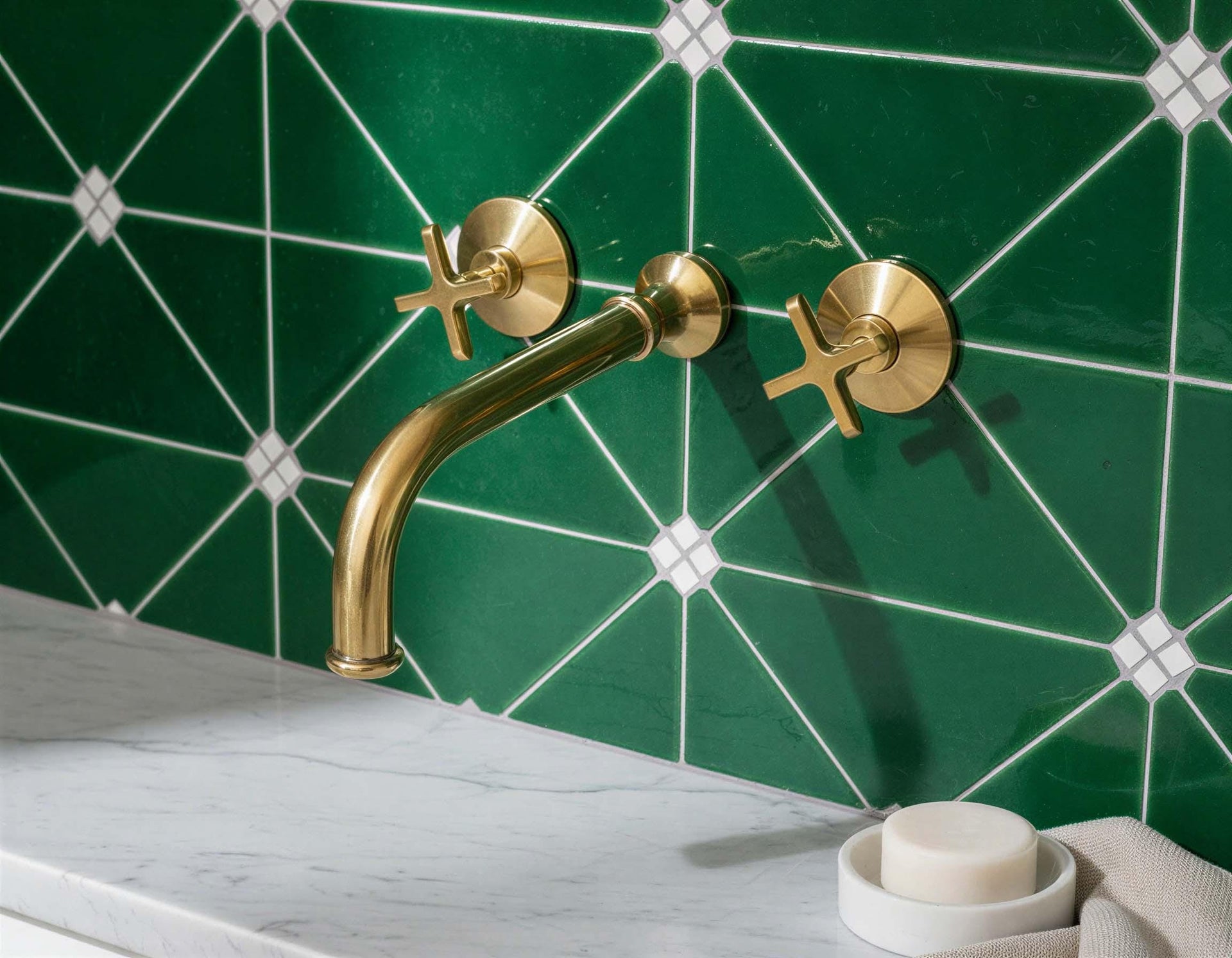 Gold faucet on a green tiled wall with a white soap dish and bar.