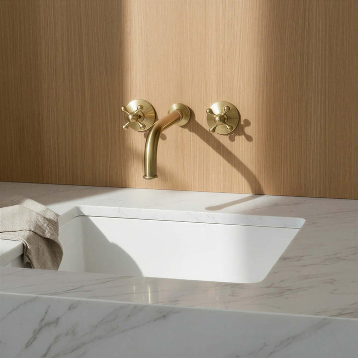 Gold faucet on a white sink with a wooden wall background