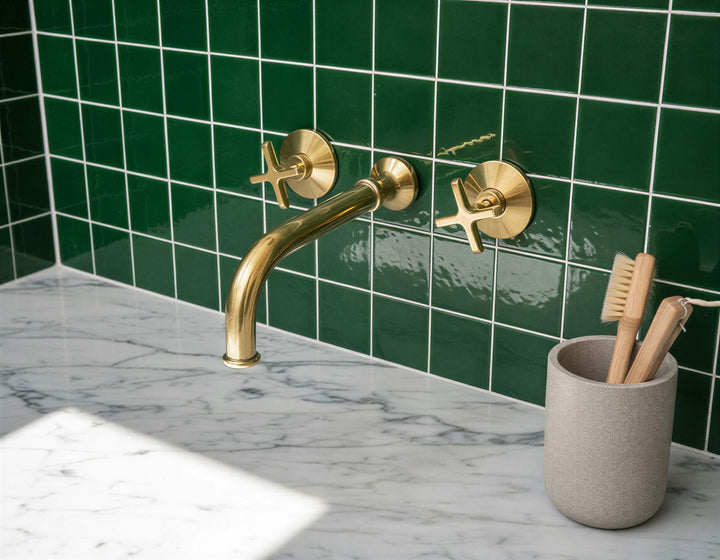 Gold faucet on a marble countertop with green tiled wall