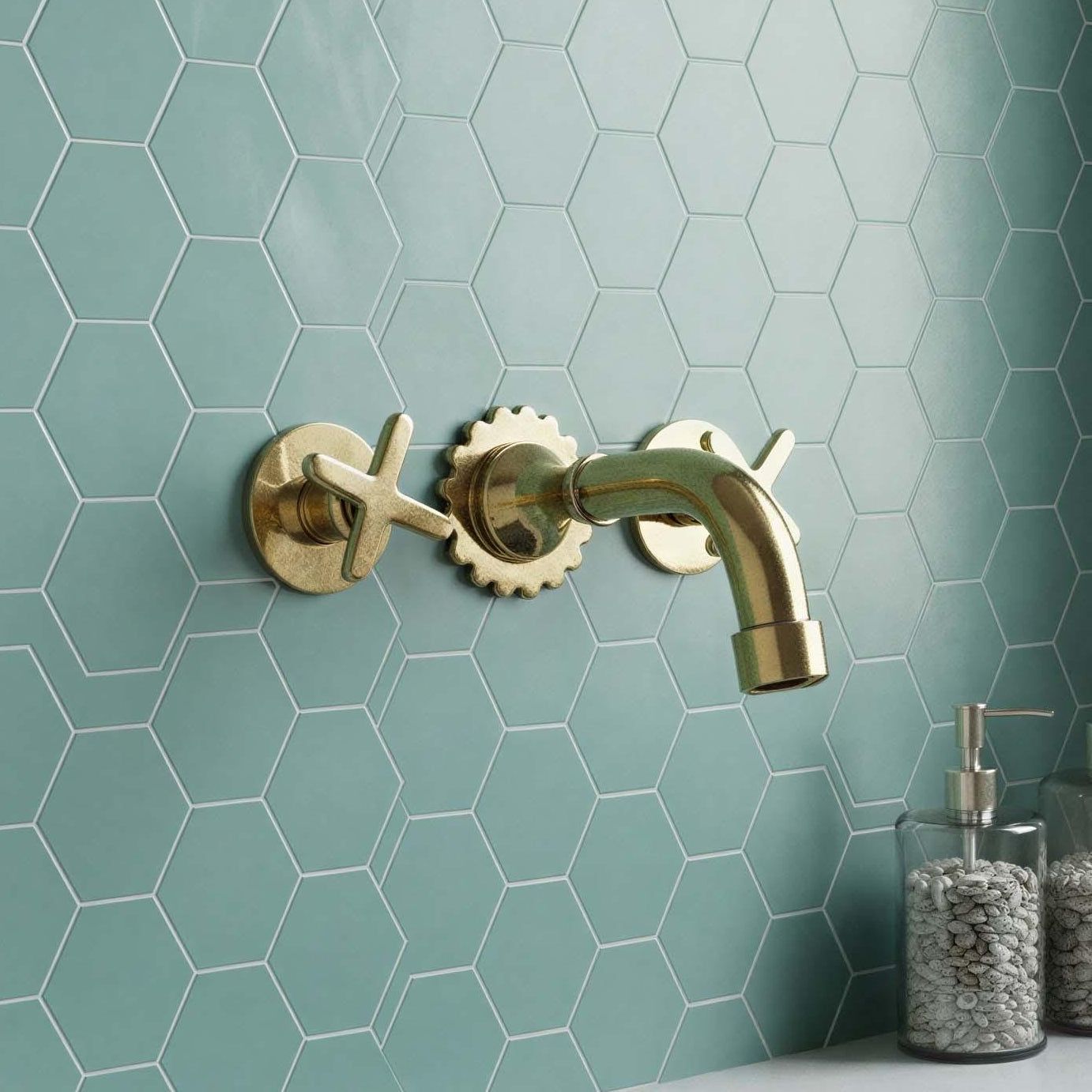 Bathroom sink with gold faucet against a green tiled wall