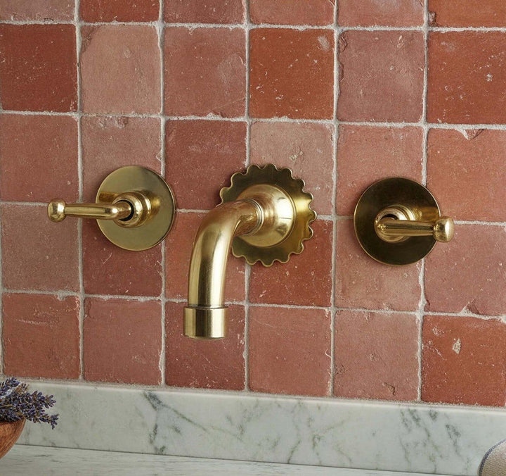 Gold bathroom faucet and handles on a tiled wall