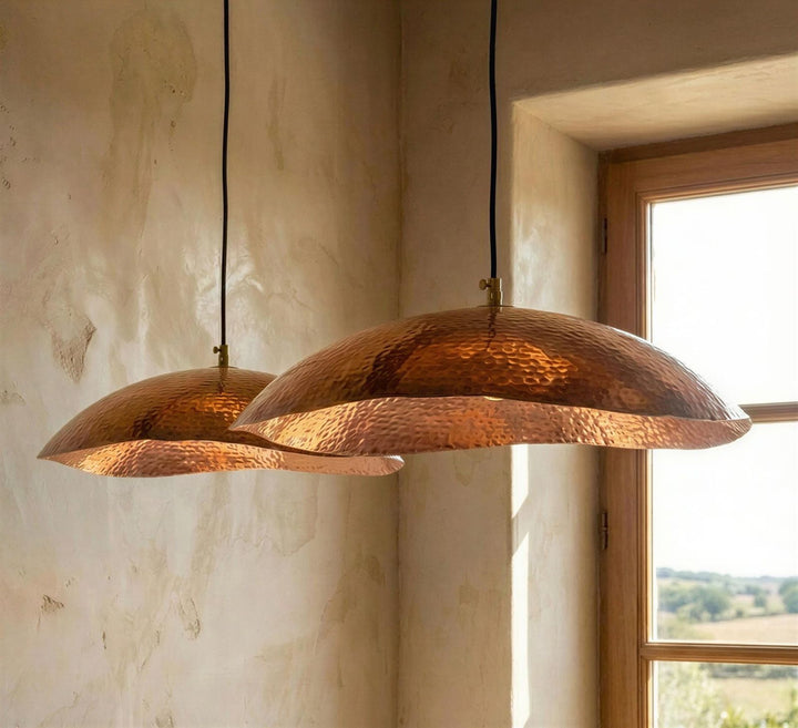 Two copper pendant lights hanging in a room with a window in the background.