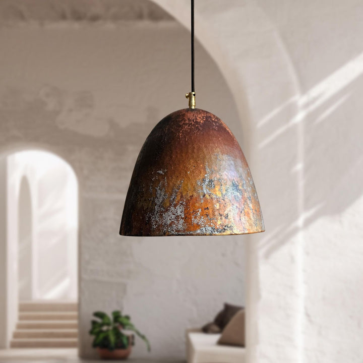 Rust-colored pendant light hanging in a room with white walls and a plant.